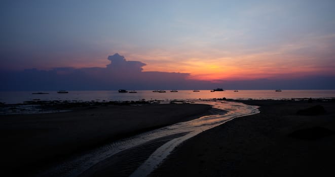 Colorful sunset above the river flowing into the sea. Plenty of boats in the water