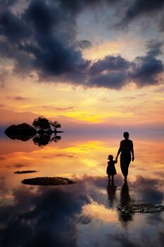 Silhouette of mother and daughter going into the sea sunset at the tropical island. Beautiful colorful clouds in the sky