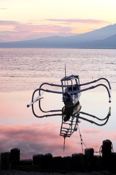 Catamaran boat at the sea in the morning with pink clouds reflected in the water