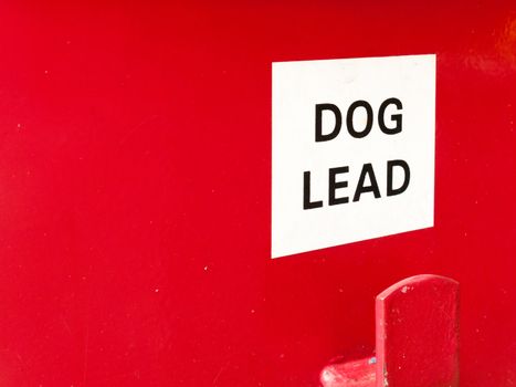 a white and red sign saying dog lead on a red bin box for litter clean nature environment animals