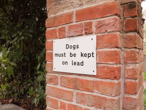 a dogs must be kept of lead white and black simple sign nailed to a brick wall on the outside near a carpark and park no people