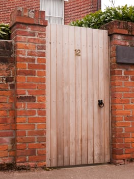 a wooden door outside closed with the number 12 on it and attached to a high wall on a house private and personal