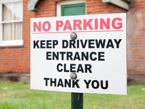 a sign outside a house saying no parking keep driveway entrance clear thank you red and white and black on post nailed screwed warning restrictions law