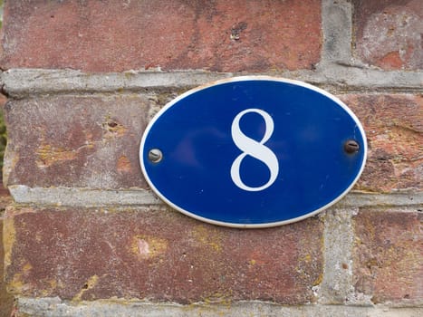 a house number plate outside blue with white number 8 oval on brick wall close up detail