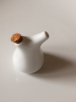 A Small And White Little Bottle of Oil with Two Holes on Spout and a Brown Wood chip Cork in its Hole Casting a Shadow on A White Background in the Kitchen Used for Cooking and Looking Decorative and Neat in The UK