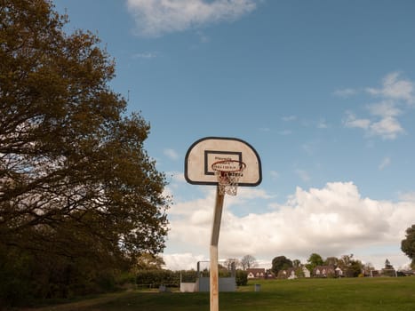 A Single Basketball Hoop in the Park with No One or Person Around, With A Red Rim and White and Black Back Board and White Net, with No One Using It, During the Day Time in the Sunlight in Spring in the UK