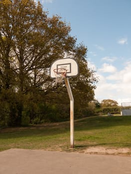 A Single Basketball Hoop in the Park with No One or Person Around, With A Red Rim and White and Black Back Board and White Net, with No One Using It, During the Day Time in the Sunlight in Spring in the UK