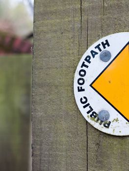 Half of A Sign on A Wood Post Saying Public Footpath with Semi-Circle and Yellow Arrowhead Leading to the Left to the Pathway in UK in Spring