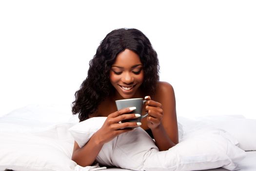 Beautiful happy smiling african woman with delicious coffee tea waking up in white bed.