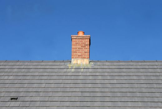 Gray tile roof and chimney on house with blue sky background.