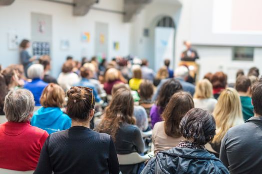 Male speaker giving presentation in lecture hall at university workshop. Audience in conference hall. Rear view of unrecognized participant in audience. Scientific conference event.