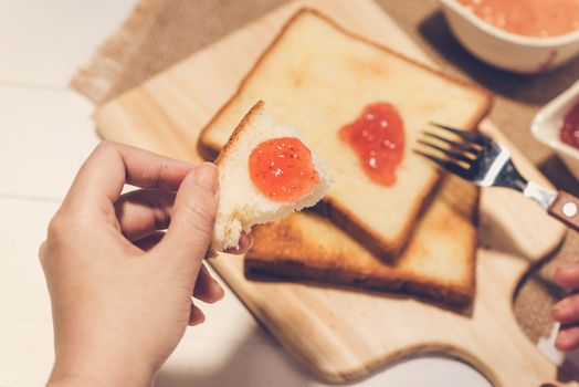 Asian woman eating bread with strawberry jam for breakfast. Focus on hands.