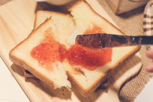 Asian woman eating bread with strawberry jam for breakfast. Focus on knife