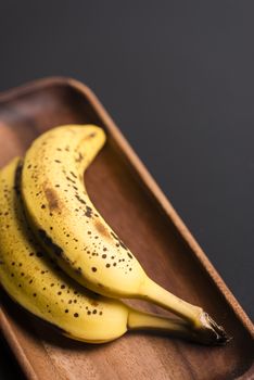 Two organic bananas in a wood sish over a black board.