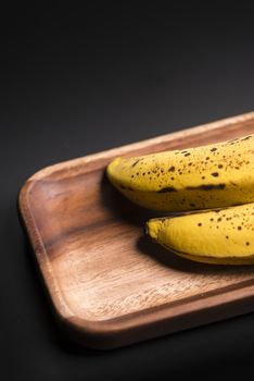 Two organic bananas in a wood sish over a black board.