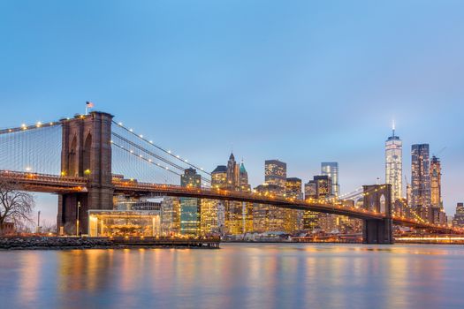 Brooklyn bridge and New York City Manhattan downtown skyline at dusk with skyscrapers illuminated over East River panorama. Panoramic composition.