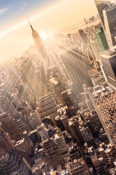 New York City. Manhattan downtown skyline with illuminated Empire State Building and skyscrapers at sunset. Vertical composition. Warm evening colors. Sunbeams and lens flare.