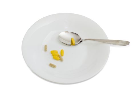 Multivitamins in the form of tablets and dietary supplements in the form of capsules on the white dish and spoon on a light background
