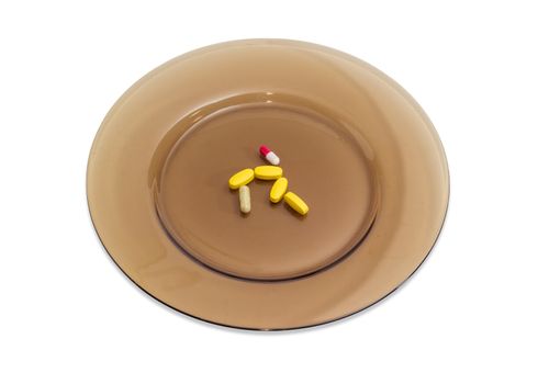 Several yellow tablets of the multivitamins and different dietary supplements in the form of capsules on the big dark glass dish on a light background
