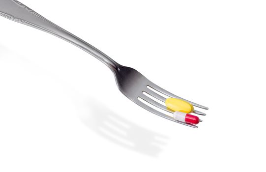 Yellow tablet of the multivitamins and capsule of the dietary supplements on the stainless steel fork closeup on a light background
