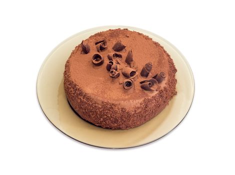 Whole round chocolate cake decorated with chocolate chips and sprinkled with cocoa powder on the dark glass dish on a light background
