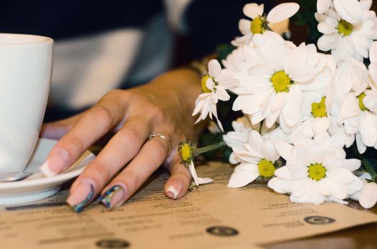 Perfect woman's hands a touch the cups with a bouquet of chamomiles, drink coffe in cafe at the weekend on the walking