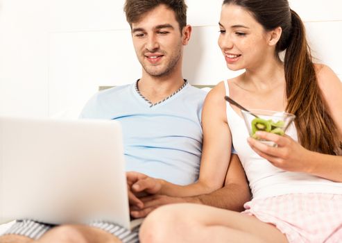 Young couple siting on bed working and eating breakfast