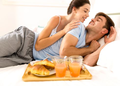 Young couple lying on the bed with breakfast on bed 