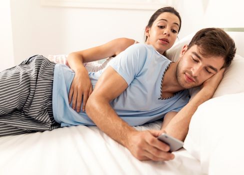 Addicted young man on bed texting  while woman looks angry