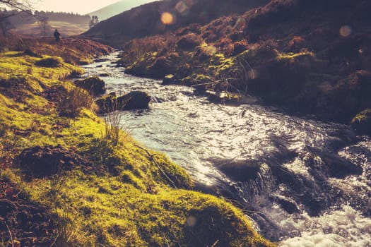 Retro Filtered Photo Of A Man Hiking In The Rugged Scottish Countryside Beside A Stream