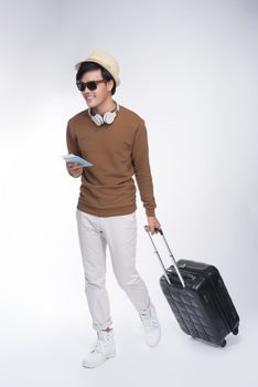 Full length of young tourist asian man holding passport with suitcase over grey background