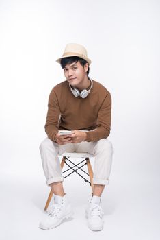 Smart casual asian man seated on chair, holding smartphone in studio background