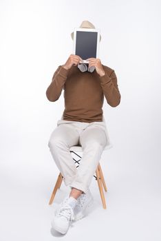 Smart casual asian man seated on chair, showing digital tablet screen in studio background