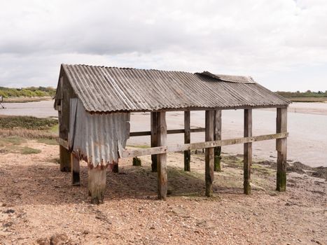 an old and abandoned sea shack shed decaying and rotting in the sun as seen from the side and back at the beach and seafront made of wooden and metal