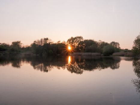 beautiful sun set over a lake in spring with a sun globe orb tree reflections in lake pond