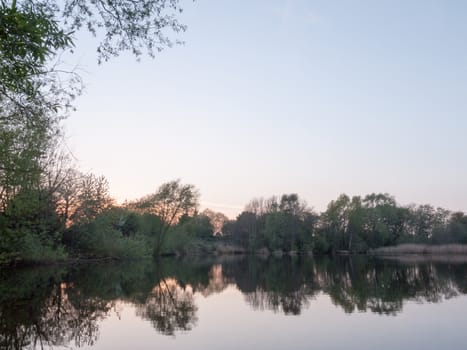 sunsetting over a lake as the trees around are reflected in the water in spring time in the countryside