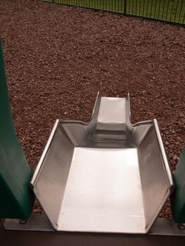 a close up shot of a metal slide in a child's playground with bark wooden chips for safety, accident, no people shining metal, dangerous and fun for children and parents in summer and spring