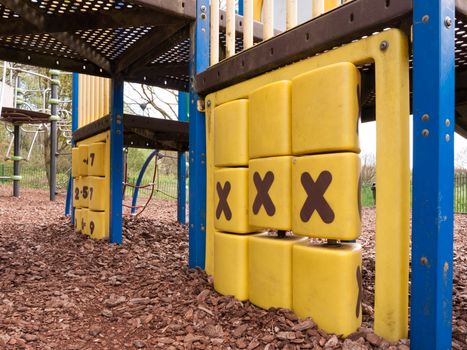 a playground park child's toy of crossed and zeros with three x symbols of black on yellow turning blocks before climbing frame no people or children in light playing