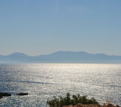 The sun's rays are reflected in the blue water of the Mediterranean Sea near the rocky coast of Turkey