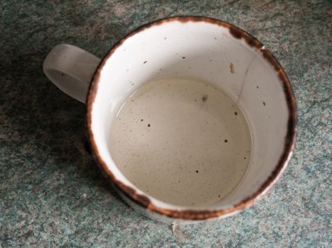 A Small White and Black Spotted Cup with A Rusty Rim and with A Small Bit of Liquid, water, and Oil in the Bottom Base as Seen From Above Overhead in UK Kitchen for Cooking