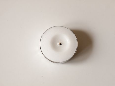 A Small White Wax Candle in A Circle Metal Base with Black Wick and No Flame, casting a Shadow on a White Background and Up Close Overhead in UK