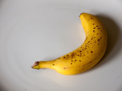 A Single Brown Spotted Yellow Banana Laying Down and Casting a Shadow on a White Background in the Kitchen, Healthy Eating and Fruit in UK