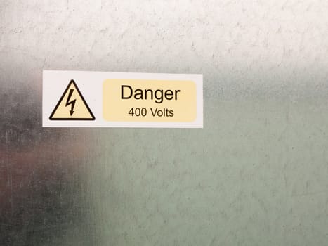 an electric bolt in triangle white yellow and black safety caution sign warning saying danger 400 volts attached to a metal wall background danger