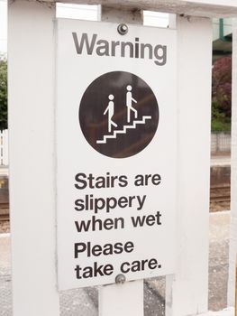 a warning sign saying stairs are slippery when wet please take care near train track bridge steps up careful safety caution advisory