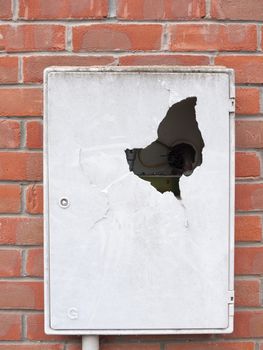 a meter box broken into outside with cracked dent hole old danger electric gas box on brick wall on house crime vandalism teenagers thugs smashed dangerous live