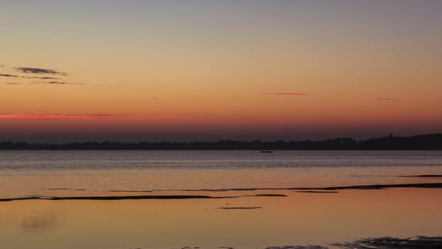 Beautiful sunset over calm lake, boat silhouette