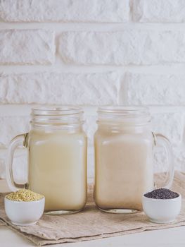 Close up view on two mason jar with vegan milk from sesame seeds and poppy seeds on white table. Copy space. Vertical.