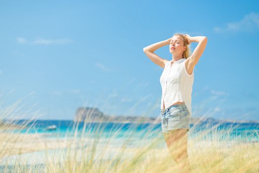 Relaxed woman, arms rised, enjoying sun, freedom and life an a beautiful beach. Young lady feeling free, relaxed and happy. Concept of vacations, freedom, happiness, enjoyment and well being.