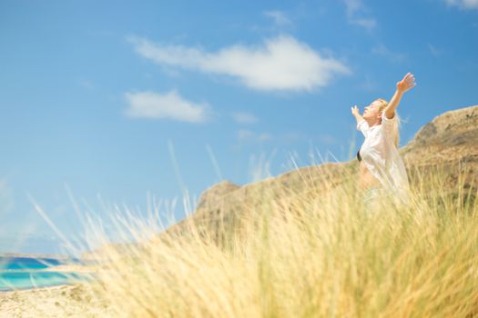 Relaxed woman, arms rised, enjoying sun, freedom and life an a beautiful beach. Young lady feeling free, relaxed and happy. Concept of vacations, freedom, happiness, enjoyment and well being.