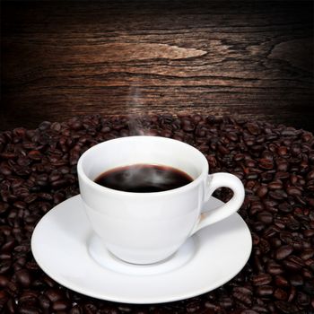 Black coffee in cup and coffee beans with smoke on old wood background.